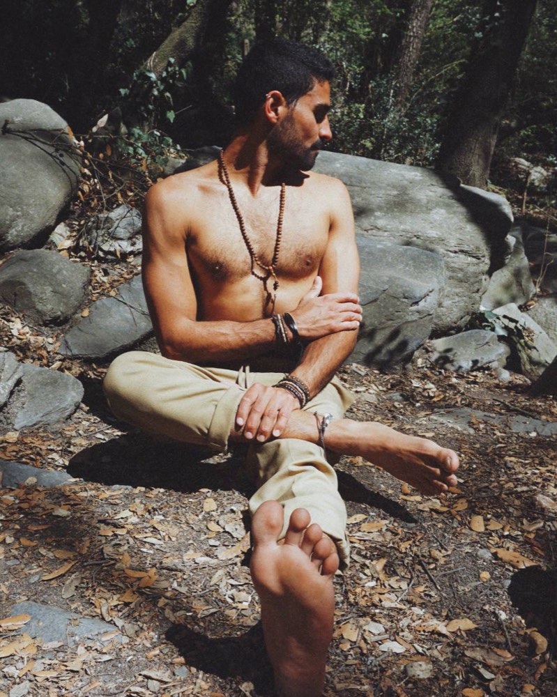 Stefano Bonanno sentado descalzo entre rocas en un bosque, mirando hacia un costado.